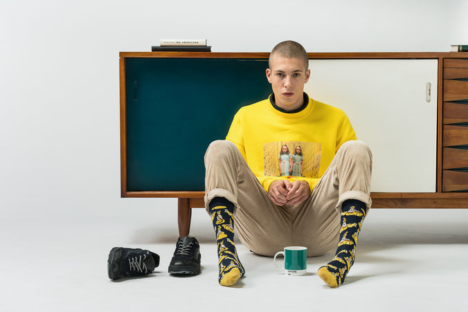 A man sitting on the floor with a cup, wearing custom shoes.