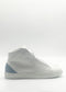 The MH0120 White & Artic Blue sneakers boast a white high-top design adorned with a light blue heel accent, masterfully handcrafted in Portugal from premium Italian leather and presented against a plain backdrop.