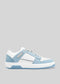 The M0011 by Serifo is a white and light blue sneaker with a flat sole, featuring a lace-up design and accented with perforated details and light blue suede patches on a gray background. This retro-future sneaker is handcrafted in Portugal using premium Italian leathers for ultimate quality.