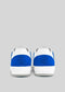 Rear view of the Build retro-future sneakers featuring white premium Italian leathers with blue accents on the heel and a geometric logo embossed on the back of each shoe, handcrafted in Portugal and set against a plain gray background.