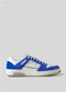 A DiVERGE x BUILD low-cut sneaker, in white and blue with a white sole, featuring the "Build" brand name on the side, handcrafted in Portugal.