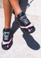 Person wearing black and pink sneakers with white laces, standing on a sunny outdoor surface. L0015 by Becas are ethically made to order from premium Italian leathers.