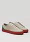 Introducing the V43 Beige W/ Red sneakers, crafted from premium Italian leathers, featuring red soles and green accents on the heels. They are adorned with white shoelaces and showcased on a light gray background.