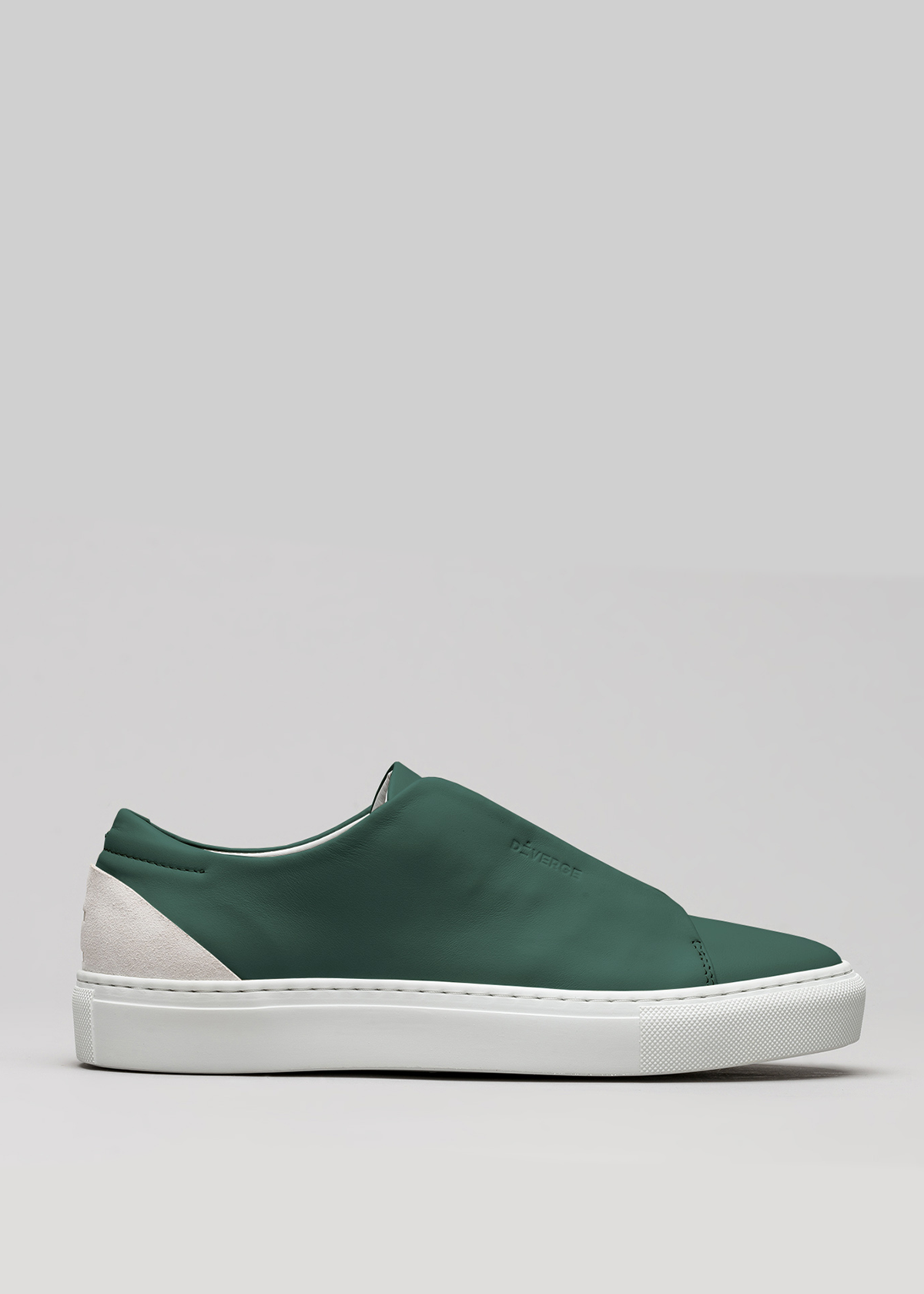 The V39 Emerald Green W/ Bone is a green slip-on sneaker with a white rubber sole and a beige suede heel accent, handcrafted in Portugal using ethical practices, shown in side view on a gray background.