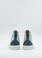 Presenting the TH0017 Blue & Green high-top sneakers: expertly handcrafted in Portugal, these sneakers boast a luxurious mix of premium canvas and soft suede. They feature stylish gray fabric with dark green accents, yellow trim, and pristine white soles, beautifully showcased from the back.