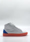 The MH0138 White & Orange is a white high-top sneaker featuring a red-orange sole and blue heel detail. It boasts a minimalist design and is meticulously handcrafted in Portugal using premium Italian leathers.