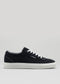 V7 Black low-top sneaker with white laces and sole, featuring visible stitching and the brand name on the side. These handcrafted sneakers boast premium canvas material.