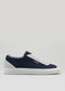 Side view of V4 Blue & Grey, a low-top sneaker in navy and white, featuring premium canvas with white laces and a flat sole, handcrafted in Portugal, set against a plain gray background.