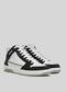 Introducing the V3 Black W/ White, a pair of high-top sneakers meticulously handcrafted in Portugal, featuring a sleek black and white design with white laces and a sturdy thick sole, all set against a plain backdrop.