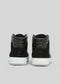 The V5 Black sneakers are a pair of black high-tops, handcrafted in Portugal using premium Italian leathers, featuring sleek white soles, and are shown from the back against a plain gray background.