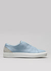 The ML0009 by Vasco is a light blue slip-on sneaker featuring a white sole, a contrasting light gray heel panel, and is handcrafted in Portugal from premium Italian leathers, all set on a plain gray background.