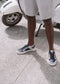 A person in gray shorts and black-and-white sneakers stands next to M0006 by Miteran on a paved surface, embodying a retro-future design vibe.