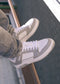 Person wearing M0009 by Nuno sneakers, handcrafted in Portugal with white and gray premium Italian leathers, sitting on a railing with gray pants visible.