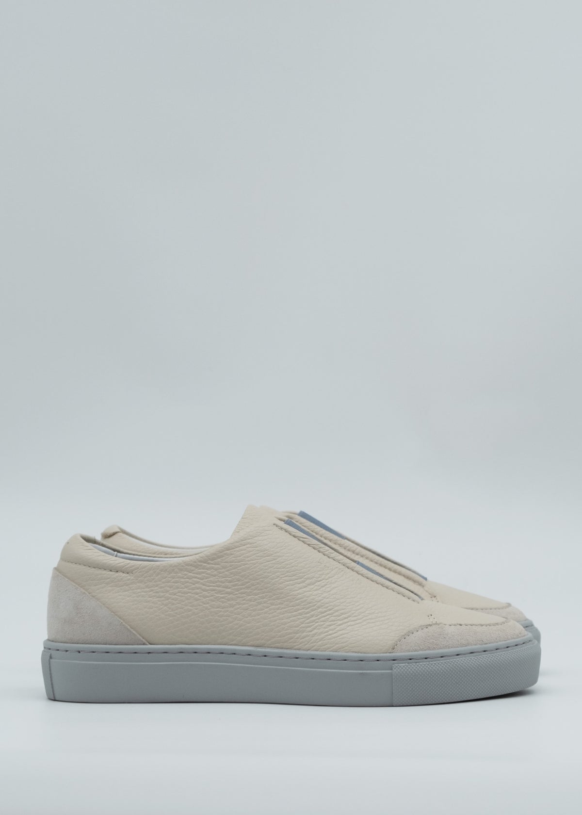 The SO0034 Beige & Blue is a beige slip-on sneaker, expertly crafted from premium Italian leathers, featuring a textured surface and a light gray sole. Set against a plain light background, each pair is meticulously handcrafted in Portugal to ensure the utmost quality and style.