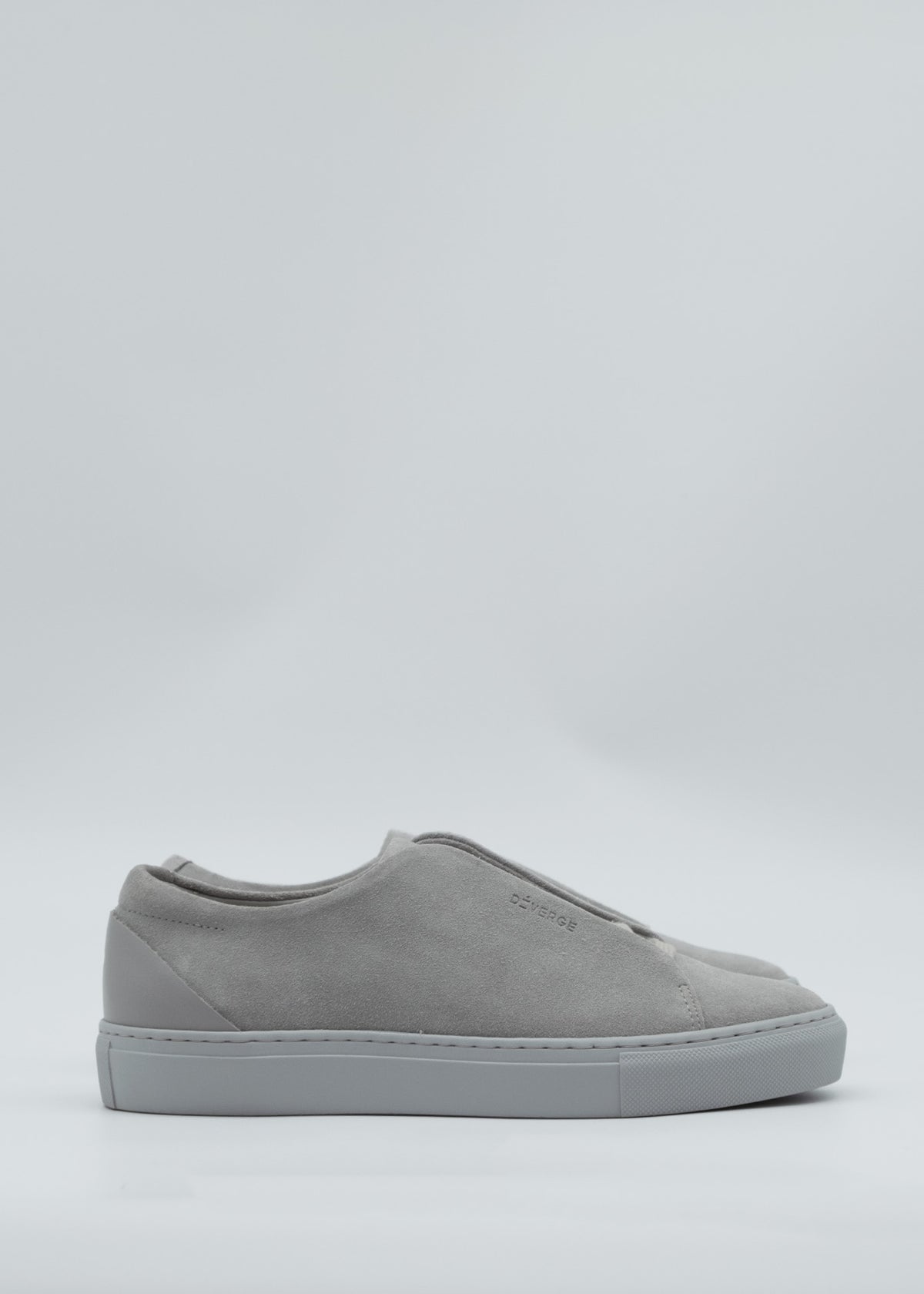 The ML0101 Grey Suede, a handcrafted slip-on sneaker from Portugal, features premium Italian leathers with a smooth upper and thick sole, elegantly displayed from the side against a light background.