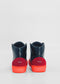 Rear view of a pair of handcrafted sneakers with a dark upper, red heel accents, and bright red soles. The product name "MH0094 Black W/ Orange" is visible on the heel. Made from premium Italian leather, these shoes are ethically made to order for those who value quality and craftsmanship.