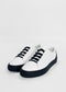A pair of ML0066 White W/ Black with black soles and black elastic bands instead of traditional laces, handcrafted in Portugal from premium Italian leathers, displayed against a plain white background.