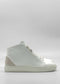 Side view of the MH0115 White Leather W/ Grey mid-top sneaker, featuring a white exterior with a beige accent at the heel, white laces, and a textured white sole, set against a plain gray background. Handcrafted in Portugal using premium Italian leathers, this shoe embodies both style and quality.