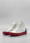 The MH0119 White W/ Electric Blue is a pair of high-top sneakers featuring white uppers, red soles, and blue accents on the heel. They are handcrafted in Portugal using premium Italian leathers and are photographed against a plain, neutral background.