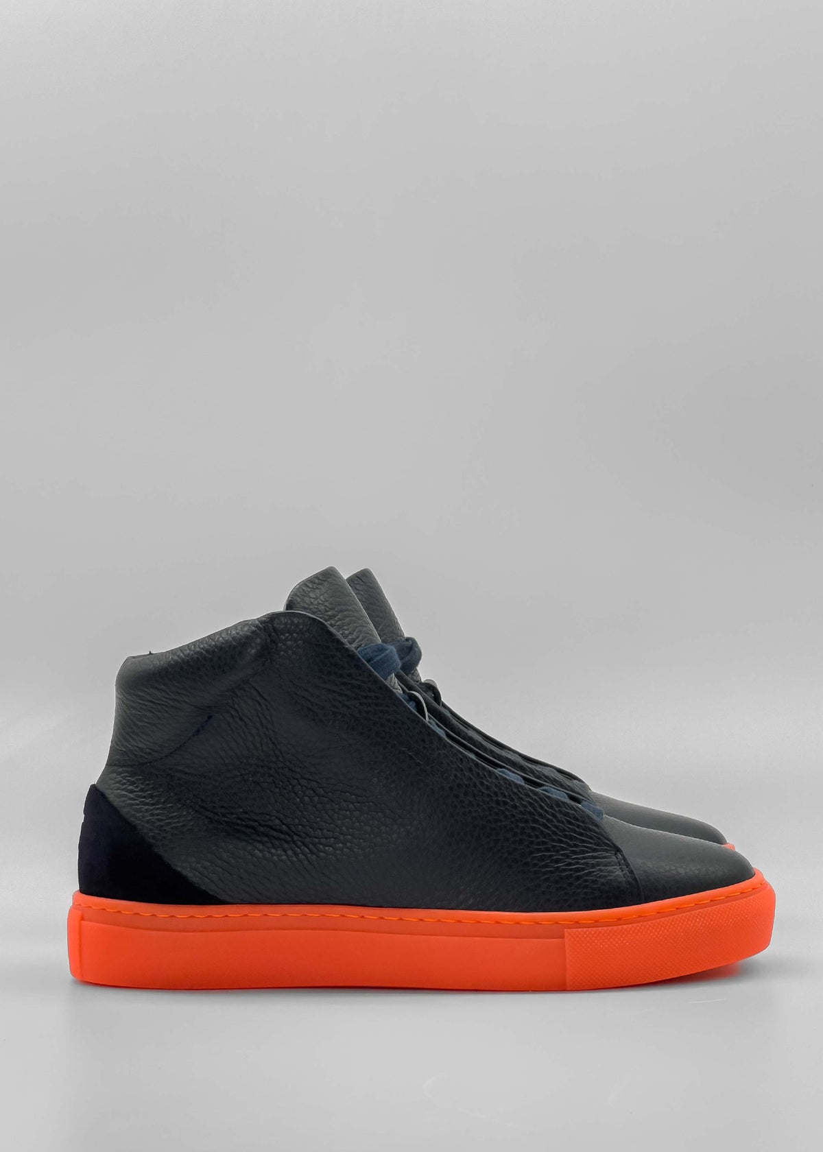 The MH0121 Grey Floater is a pair of black textured high-top sneakers, handcrafted in Portugal from premium Italian leathers, and features bright orange soles against a plain grey background.