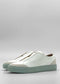 The SO0031 White Leather W/ Green shoes are a pair of white slip-on shoes featuring mint green soles and a slightly raised heel, handcrafted in Portugal and displayed against a light gray background.