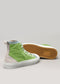 The V13 Brat, a pair of green and beige multi-layered high-top sneakers handcrafted in Portugal with white soles, are displayed; one stands upright while the other lies on its side, showcasing the honeycomb pattern on the sole.