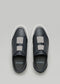 Top view of black and gray slip-on sneakers with white soles on a plain gray background. Handcrafted in Portugal, these shoes echo the quality of classic white sneakers. Inside text reads "D:VERGE," showcasing the V23 Deep Blue W/ Plaster style.