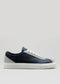 The V12 Dark Blue W/ Plaster low-top sneaker, featuring a blue and gray color scheme with white laces and a white rubber sole, is showcased against a plain background. Handcrafted in Portugal with an eye for detail, this design epitomizes style and comfort.