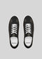 The V1 Black sneakers, a pair of low-top shoes handcrafted in Portugal from premium Italian leathers, feature white laces and are set against a gray background when viewed from above.