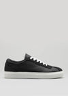 La V1 Black, una sneaker low-top nera, è realizzata a mano in Portogallo con pellami italiani di prima qualità e presenta lacci e suola bianchi su uno sfondo grigio.