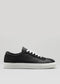 The V1 Black, a low-top sneaker expertly handcrafted in Portugal, showcases black premium Italian leathers complemented by white laces and a contrasting white sole, all set against a plain gray background.