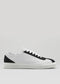 The V2 White & Black features a low-top design with white Italian leather and black accents on the toe cap, heel, and tongue. It includes white laces and a flat sole. Expertly handcrafted in Portugal, this sneaker offers a luxurious touch.