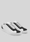 The V2 White & Black low-top sneakers, handcrafted in Portugal from premium Italian leathers, showcase a sleek design in white and black with matching white laces against a gray background.