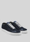 The V5 Deep Blue low-top sneakers, expertly handcrafted in Portugal from premium Italian leathers, boast a sleek design with navy and gray tones, complemented by white laces and soles against a stylish gray backdrop.