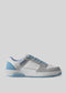 The V11 Light Grey sneaker, featuring a white and light blue design with blue laces, a white sole, and suede accents on the heel and sides, is displayed against a plain light gray background to showcase its handcrafted retro-future aesthetic.