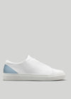 A V38 White Leather W/Artic with a blue heel accent and a white sole, viewed from the side against a plain grey background, showcases its elegance. Handcrafted in Portugal using premium Italian leathers, these customizable sneakers offer both luxury and personal flair.